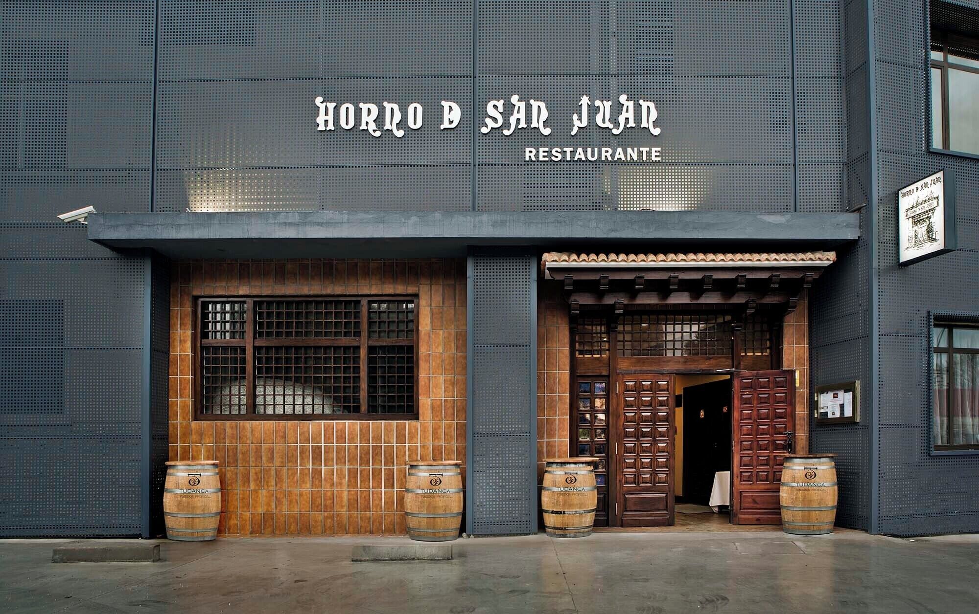 A building with a sign reading 'HORNO DE SAN JUAR RESTAURANTE' and wooden barrels in front.