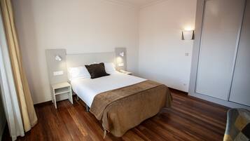 A hotel room with a single bed, a nightstand, a bedside table, a wardrobe, and a curtain.