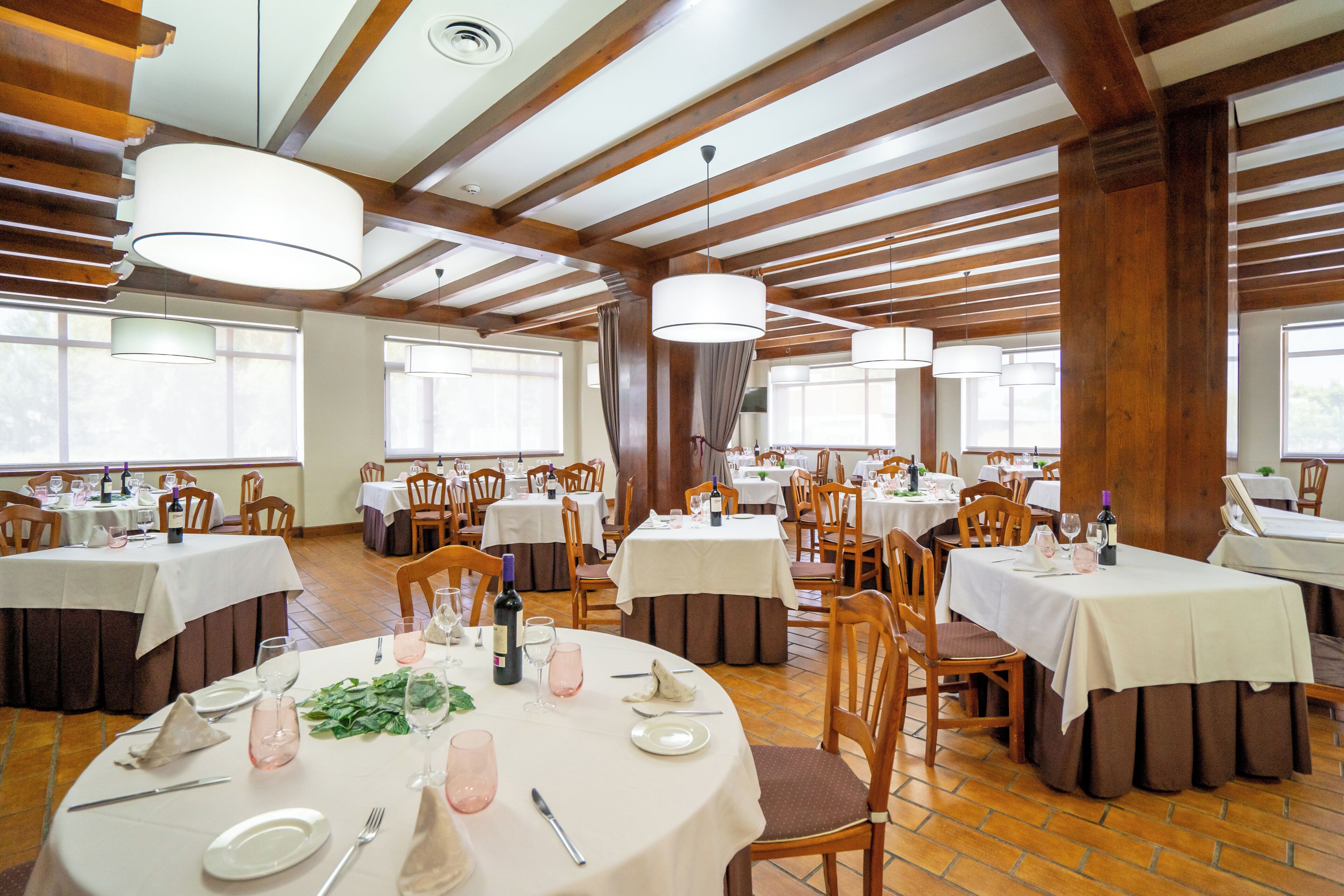A restaurant with multiple tables, wooden beams, and large windows.