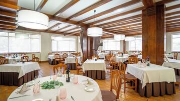 A restaurant with multiple tables, wooden beams, and large windows.