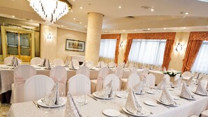 Un salón de banquetes con mesas redondas dispuestas para un evento formal, con manteles blancos y fundas para sillas a juego.