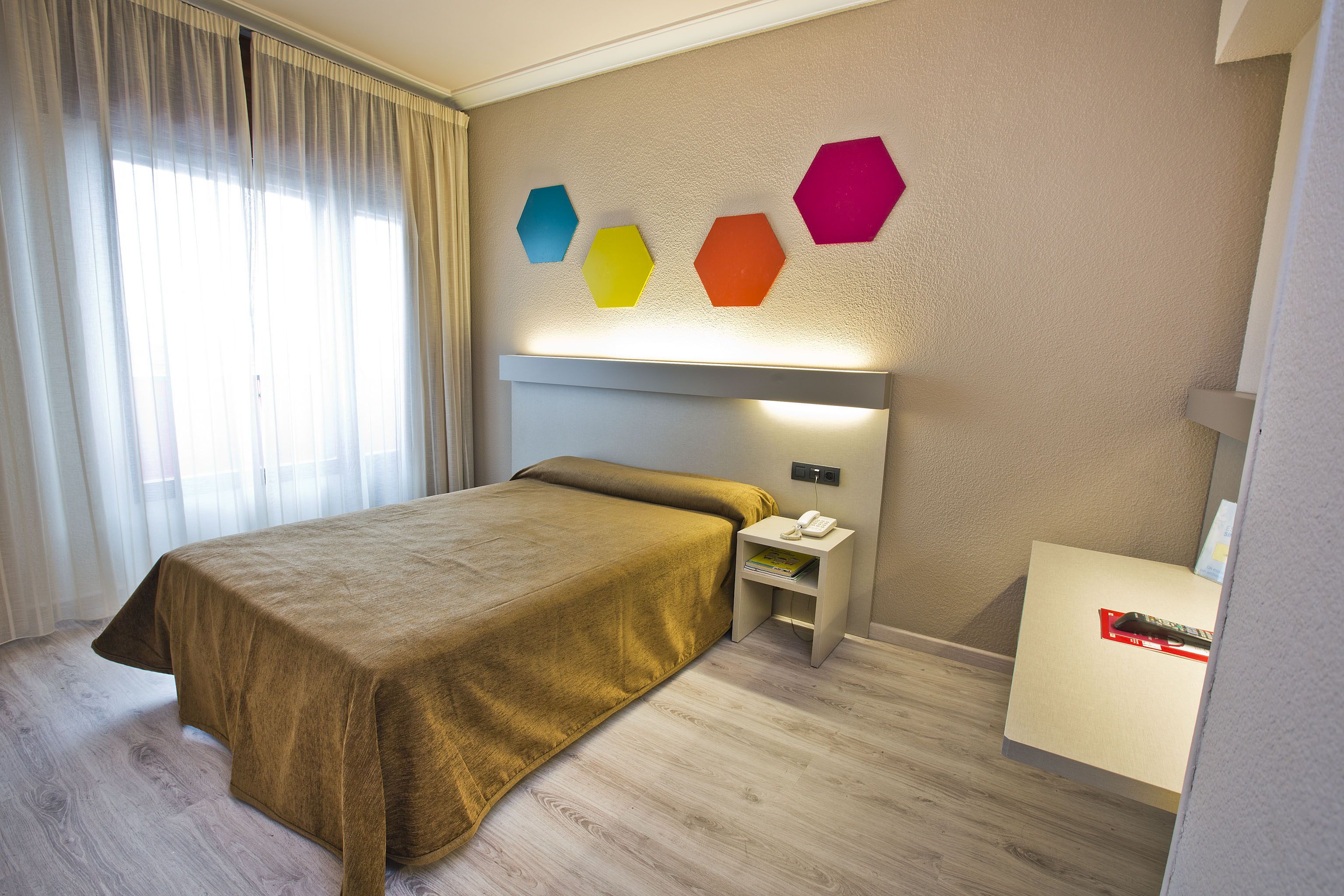 Una habitación de hotel con cama, mesita de noche y una lámpara de pared.