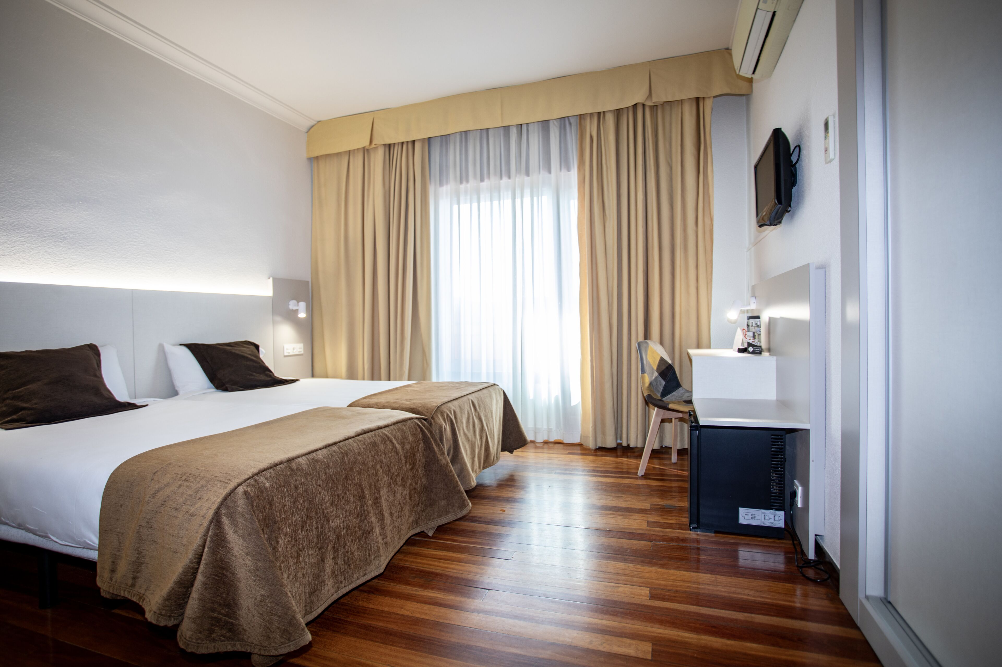 A hotel room with two beds, a desk, a chair, and a television.