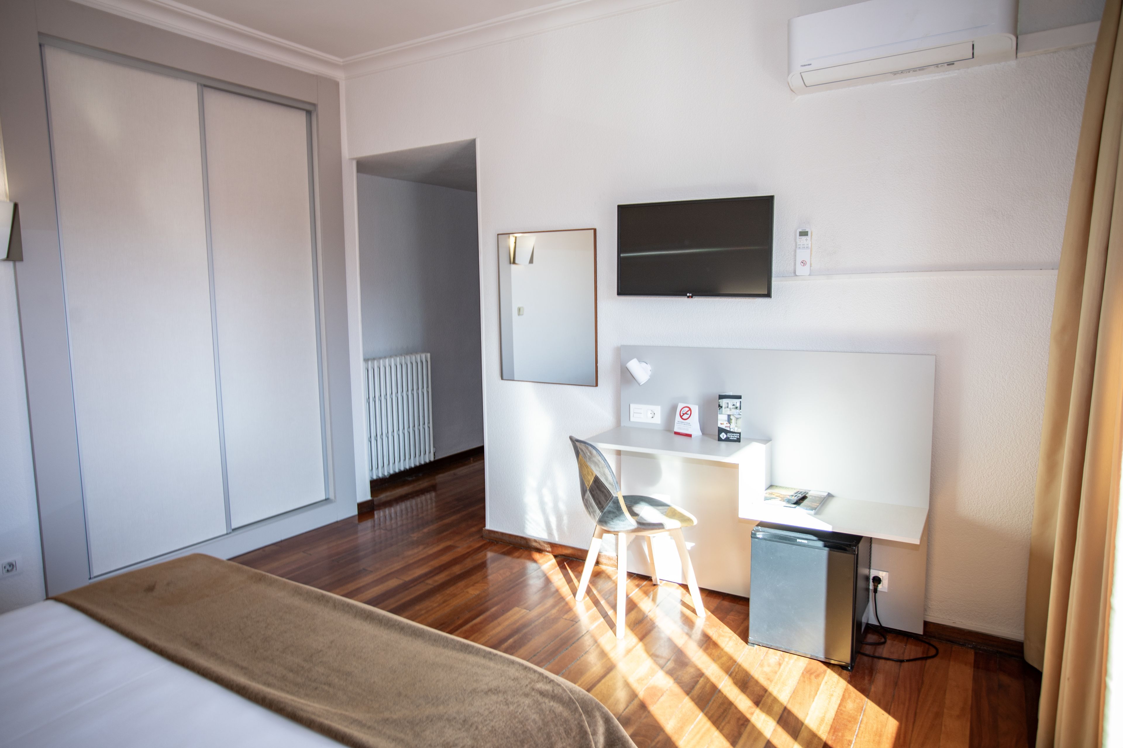 Quarto de hotel com uma cama, uma escrivaninha com cadeira, uma televisão e um radiador.