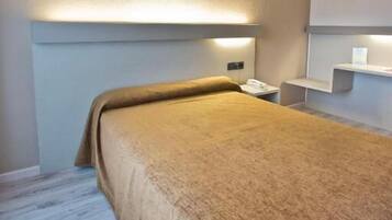 A hotel room with a bed, a bedside table, and a wall-mounted shelf.