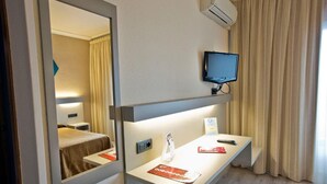 A hotel room with a bed, a bedside table with a remote control, a TV mounted on the wall, and a mirror reflecting the room. - Tudanca Miranda (Miranda de Ebro)