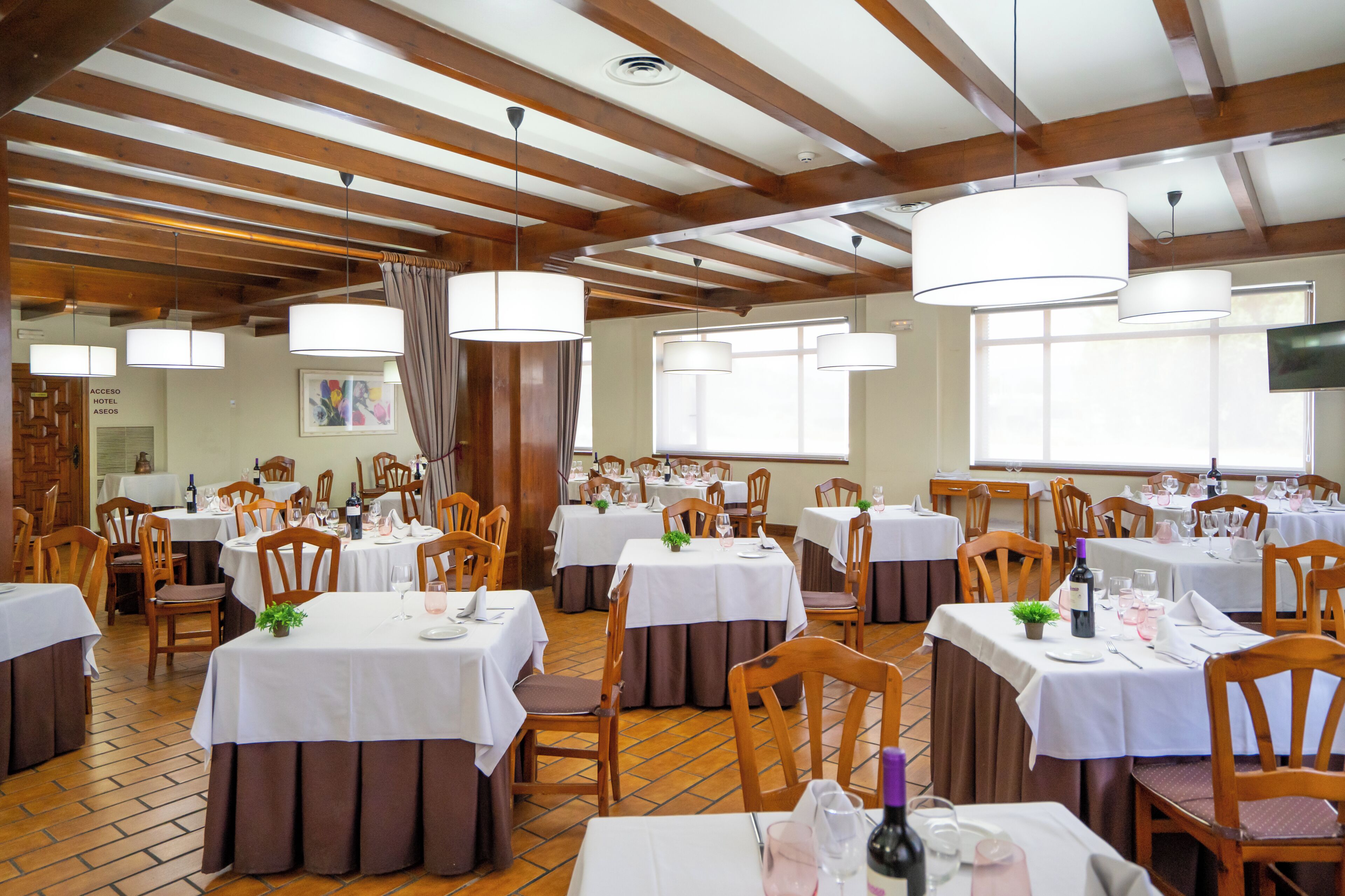 Een restaurant met meerdere tafels, houten stoelen en hangende pendelverlichting.
