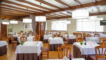 Een restaurant met meerdere tafels, houten stoelen en hangende pendelverlichting.