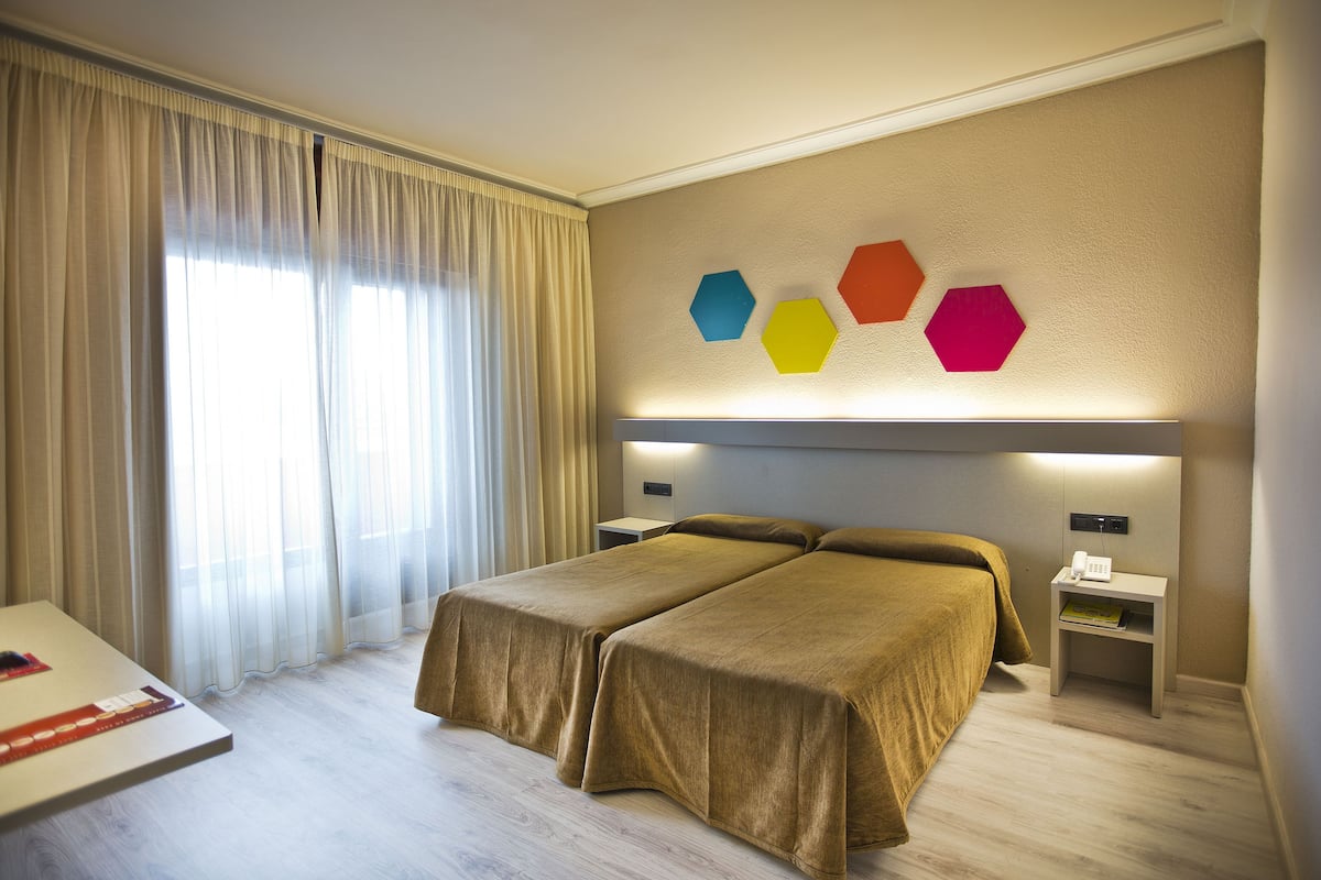 A hotel room with two beds, a bedside table with a lamp, a nightstand with a phone, and a wall with hexagonal decorations.
