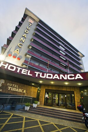 Un hotel llamado 'TUDANCA' con un letrero llamativo, una escalera que conduce a la entrada y plantas en macetas en la base.