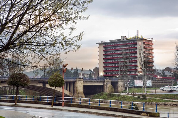 A multi-story hotel with balconies, a bridge, and a river.