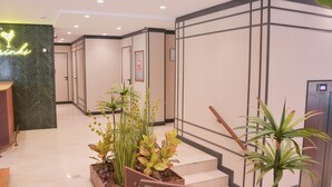 Een hotellobby met een receptiebalie, een trap en potplanten.