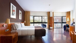 Een hotelkamer met een bed, een bureau, een stoel en grote ramen.