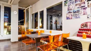 A restaurant with a modern interior, featuring clear glass chairs, a white table, and a wall adorned with framed pictures.
