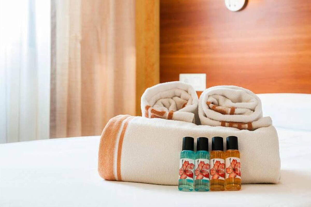 A neatly made bed with rolled towels and four bottles of bath products.