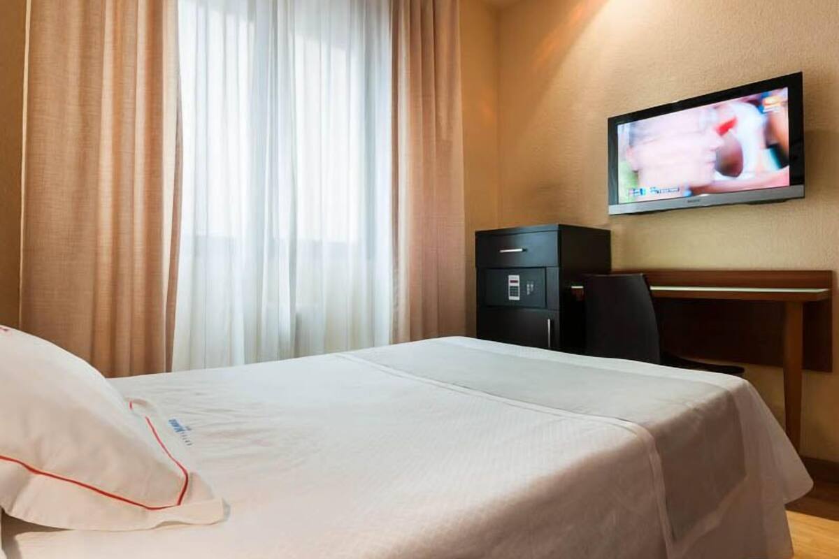 A hotel room with a bed, a desk, a television, and a safe.