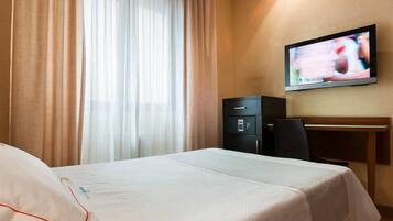 A hotel room with a bed, a desk, a television, and a safe.