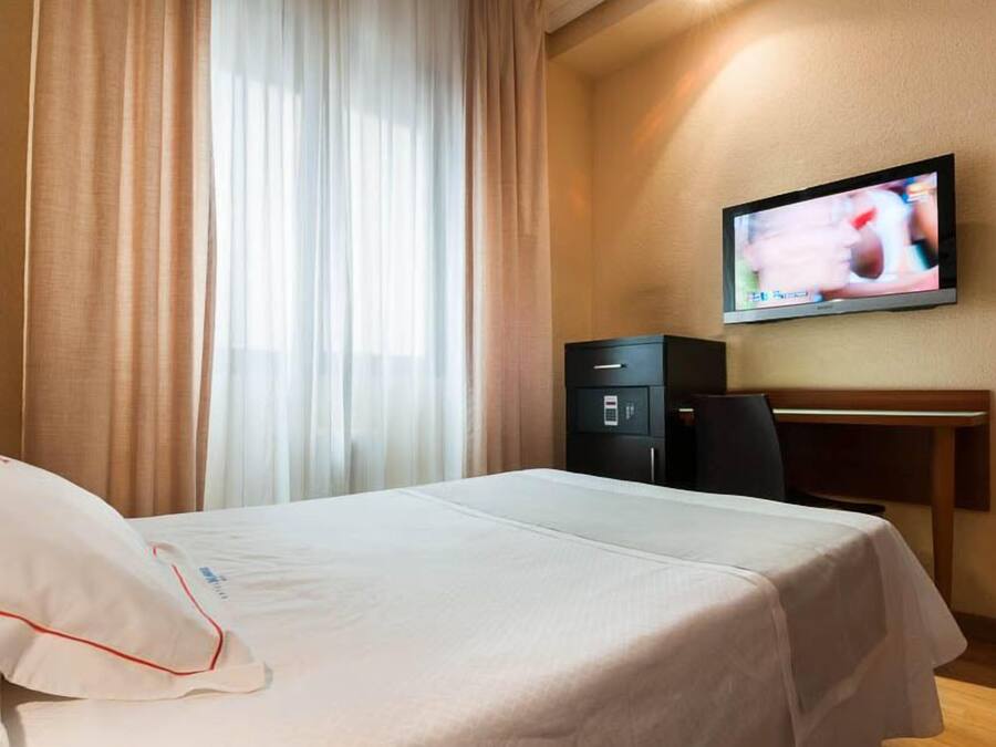 A hotel room with a bed, a desk, a television, and a safe.