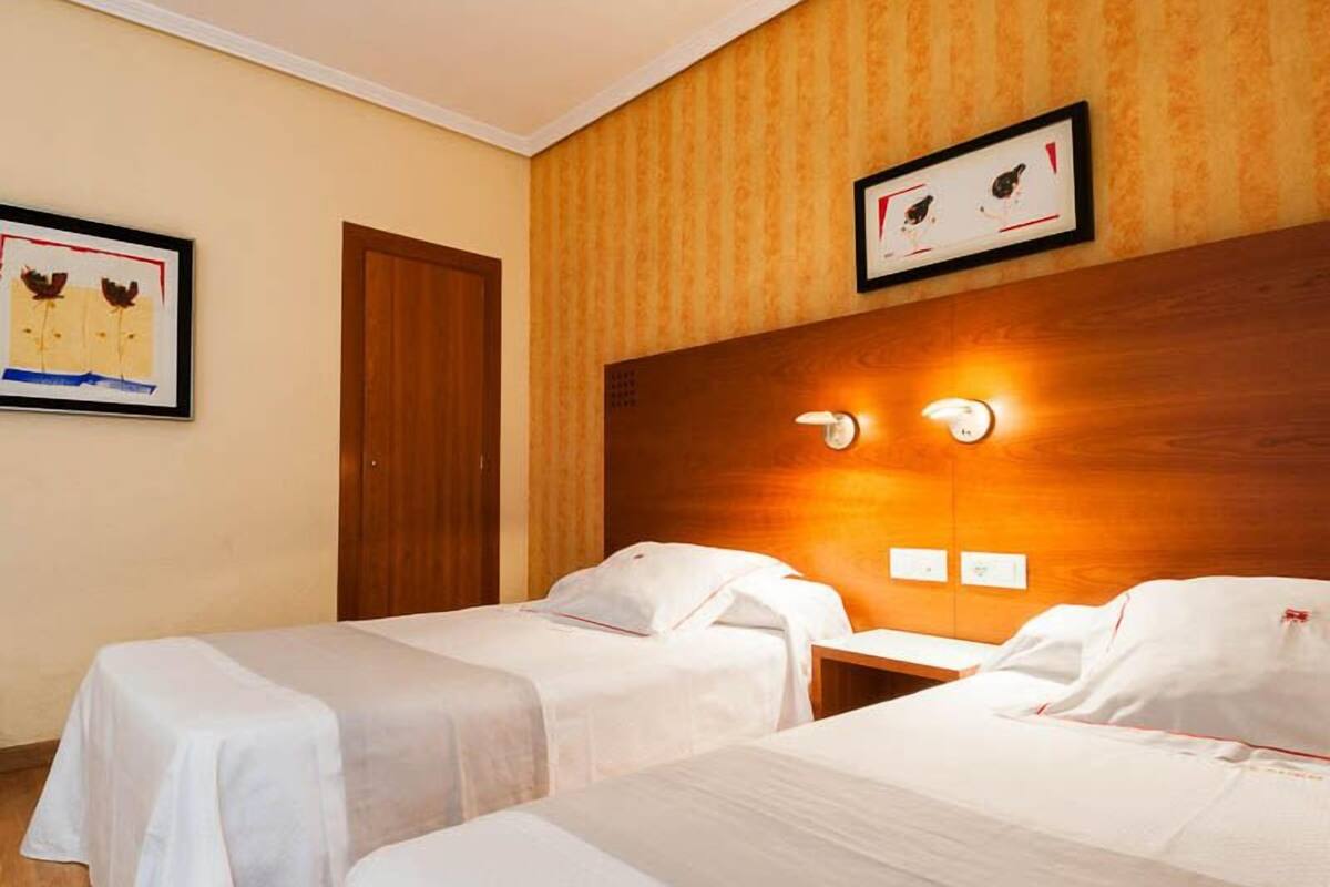 A hotel room with two single beds, a wooden headboard, a framed picture on the wall, and a door.