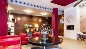 A modern lobby with red sofas, a glass coffee table, and a wooden wall with framed pictures. - Hotel Xauen (Jaén)