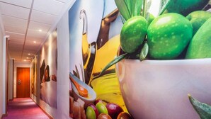A hallway with a large mural of fruits and vegetables, a wooden door at the end, and a purple carpet. - Hotel Xauen (Jaén)