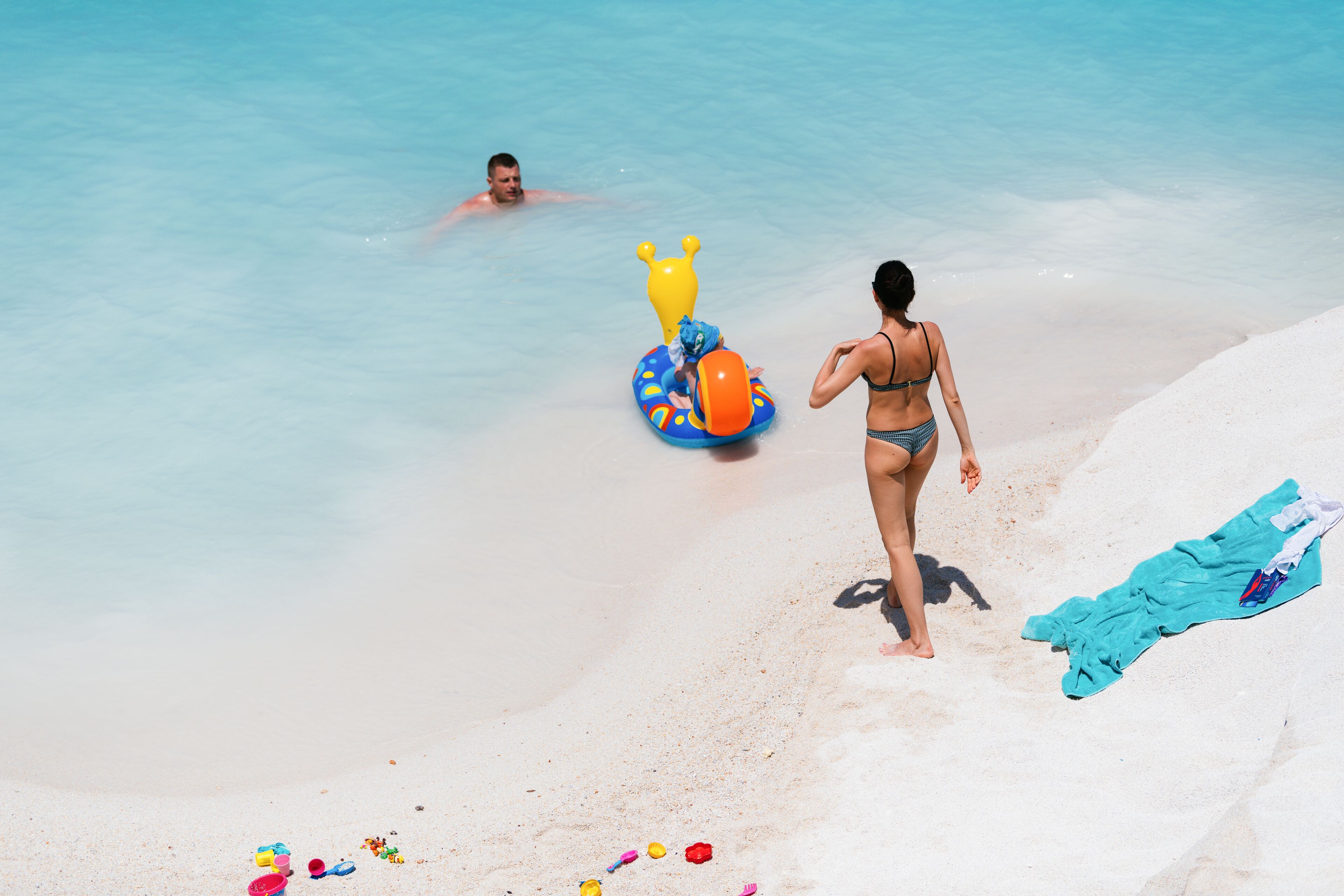 A beach scene with clear blue water, a sandy shore, and a person in a swimsuit.