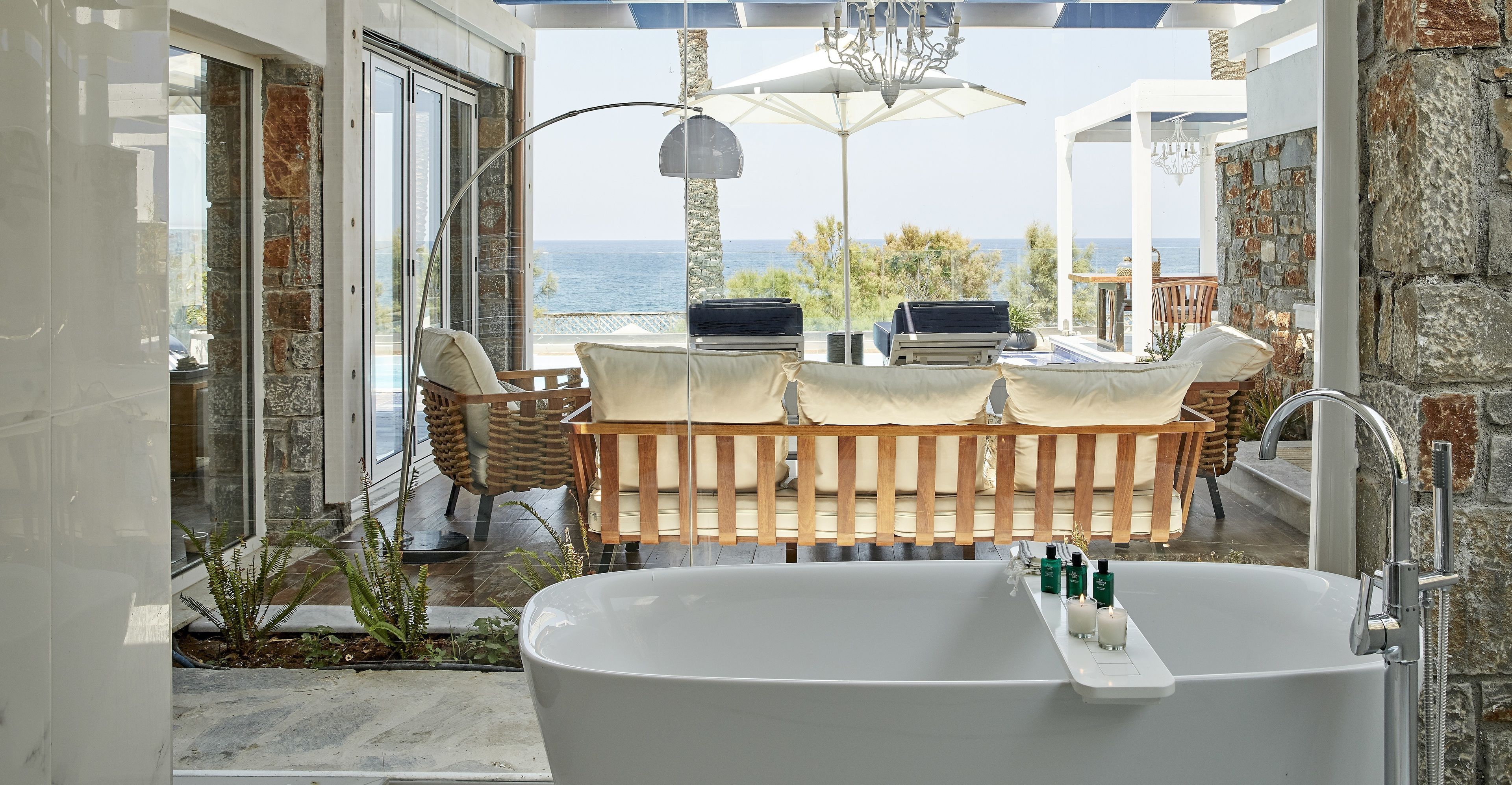 Une salle de bain moderne avec une baignoire sur pieds, un coin salon offrant une vue sur la mer et un mur en pierre.