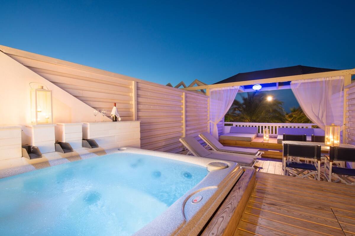 A hot tub area with a wooden deck, lounge chairs, and a seating area with a table and chairs.