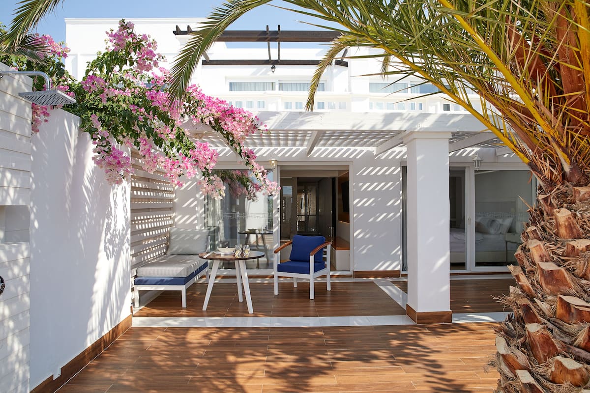 A covered outdoor seating area with a wooden floor, a blue chair, and a table.