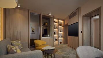 A modern living room with a sofa, armchair, and a small table. There is a TV mounted on the wall and a kitchen area with a counter and shelves.