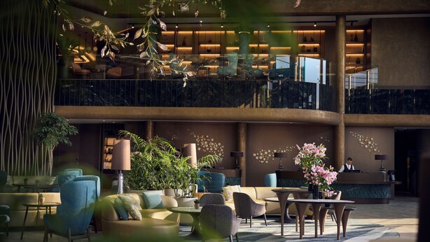 A spacious lobby with a reception desk, seating areas, and a balcony with plants.