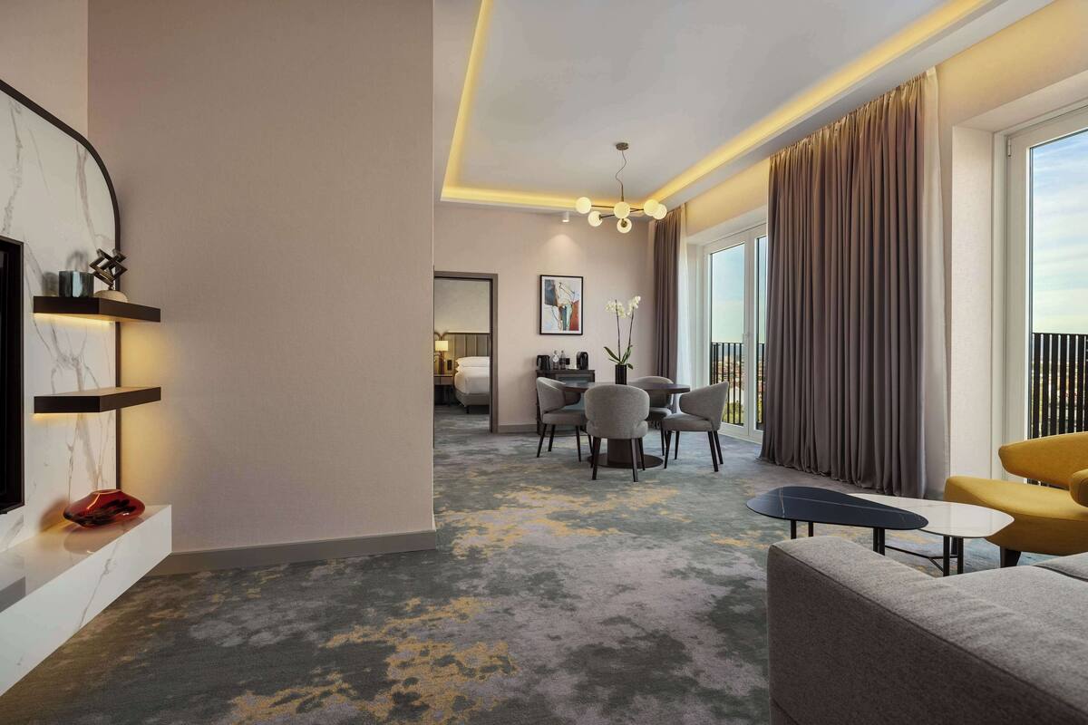 A modern hotel room with a living area, a dining space, and a balcony with curtains.