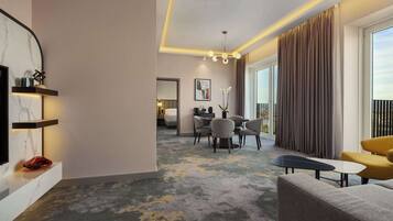 Una habitación de hotel moderna con zona de estar, comedor y balcón con cortinas.