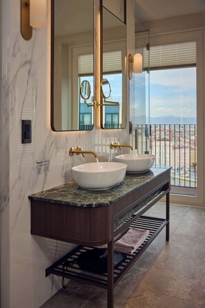 A bathroom with two white vessel sinks, a large mirror, and a view of a cityscape through a large window.