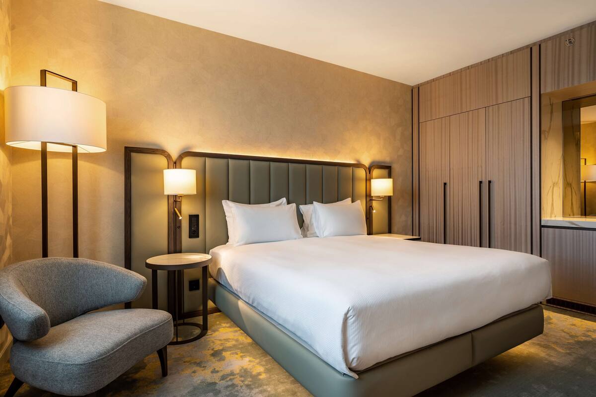 A hotel room with a large bed, a chair, a bedside table, and a mirror.