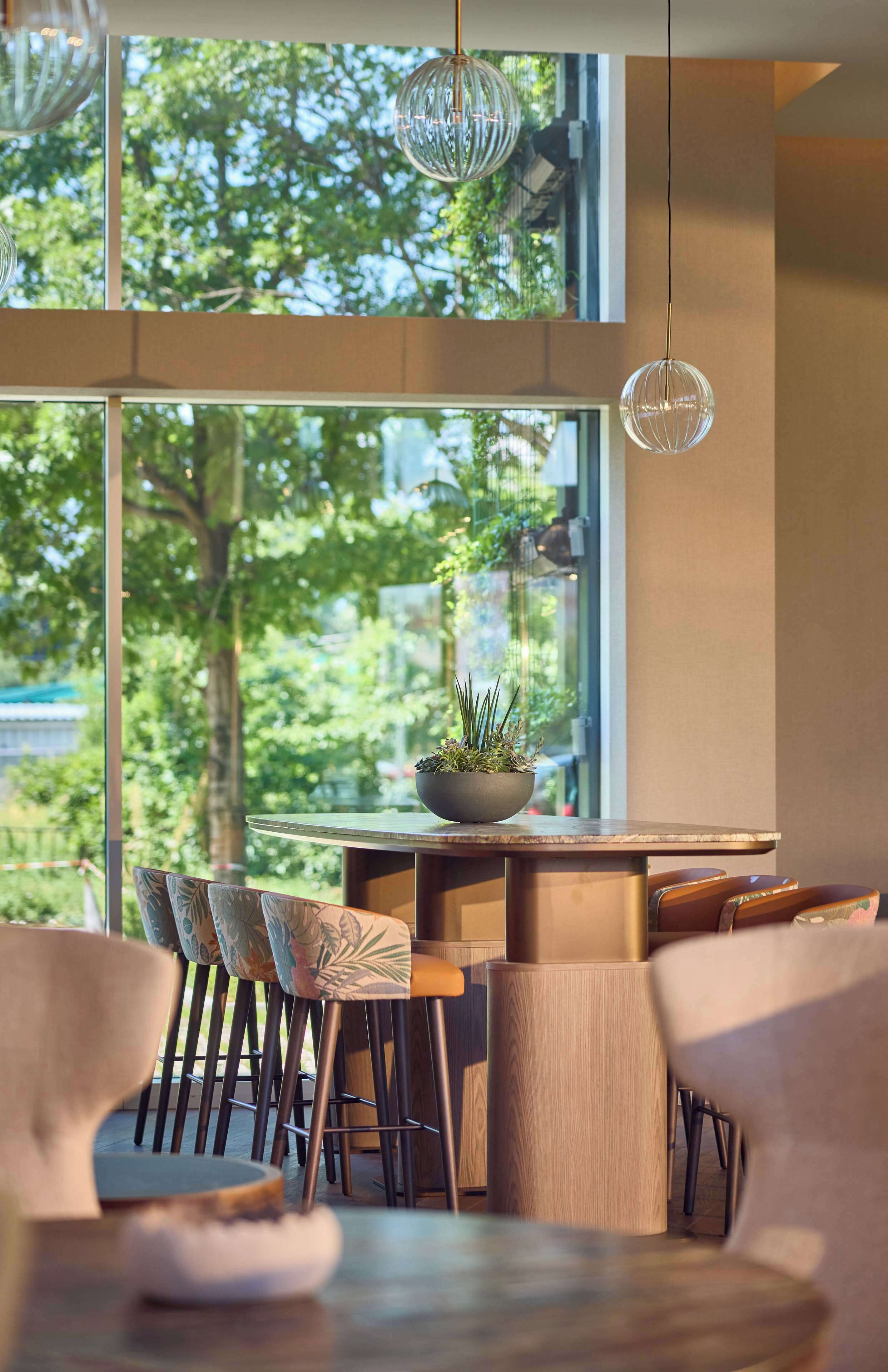 Un comedor moderno con un gran ventanal, mobiliario de madera y lámparas esféricas colgantes.