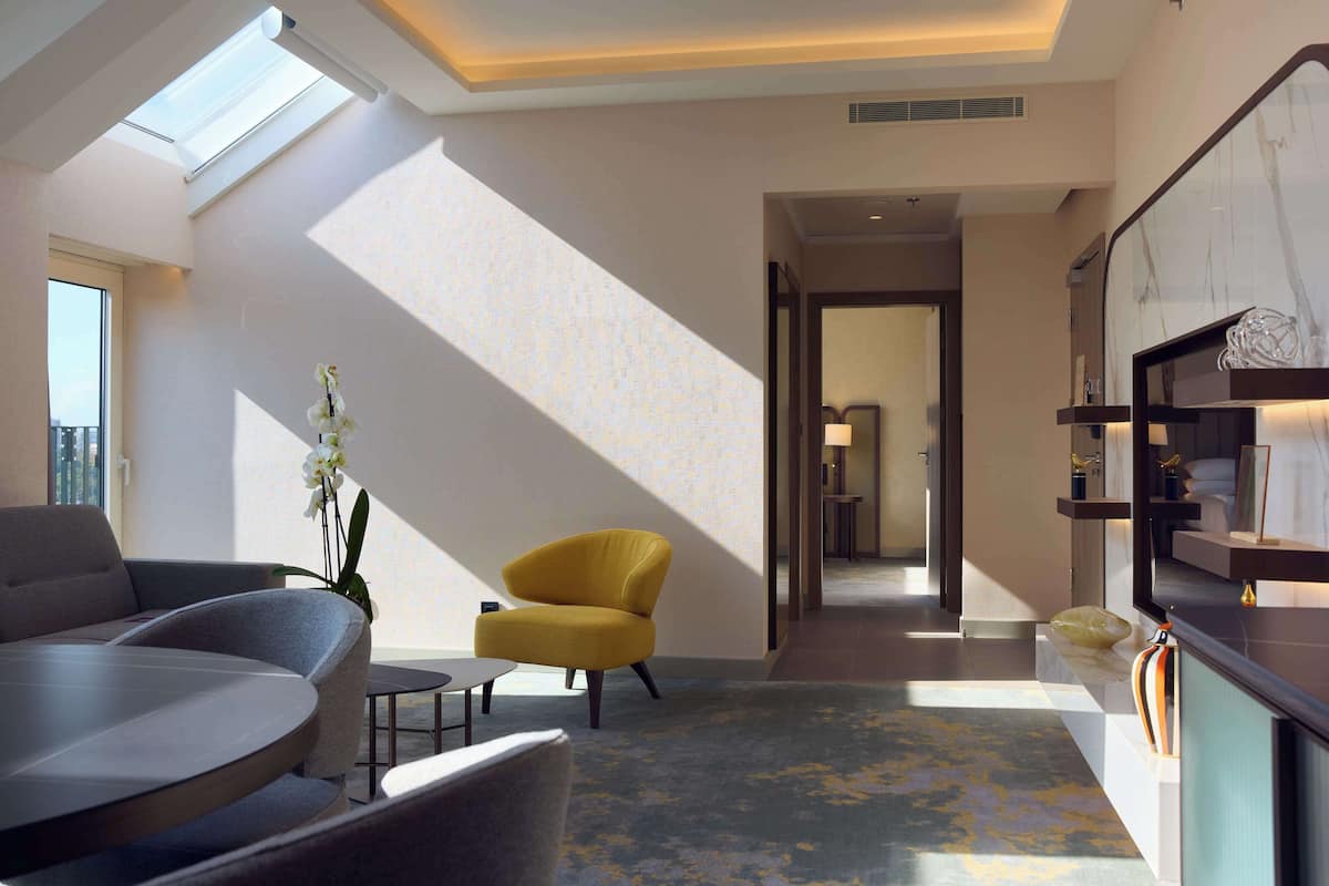 A modern living room with a sofa, a yellow armchair, and a coffee table. There is a skylight above the sofa and a view of the outside.