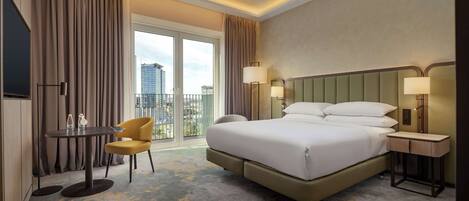 Habitación de hotel con una cama grande, un escritorio con silla, una lámpara y vistas a la ciudad a través de la ventana.