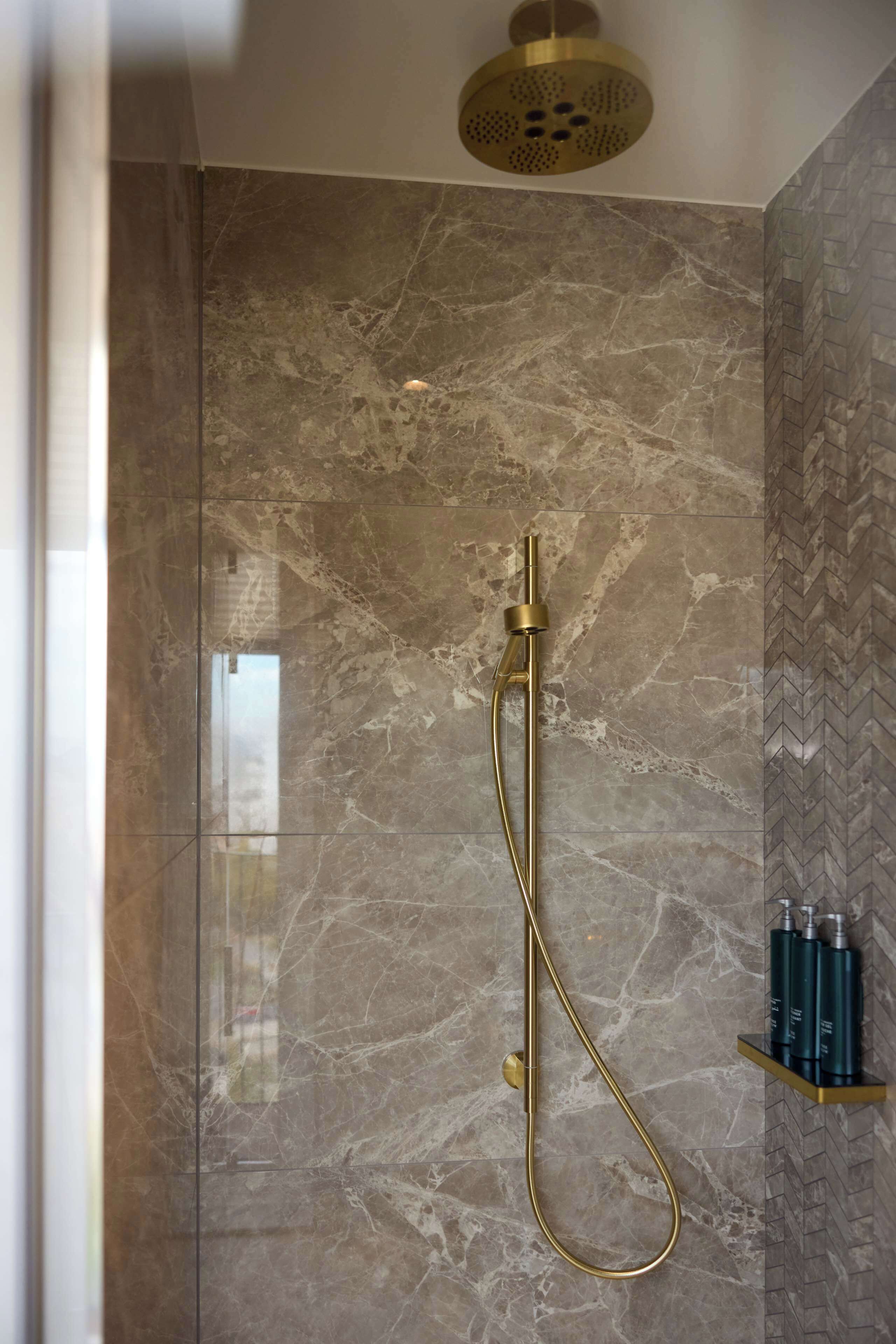 Ducha con cabezal dorado y pared de mármol.
