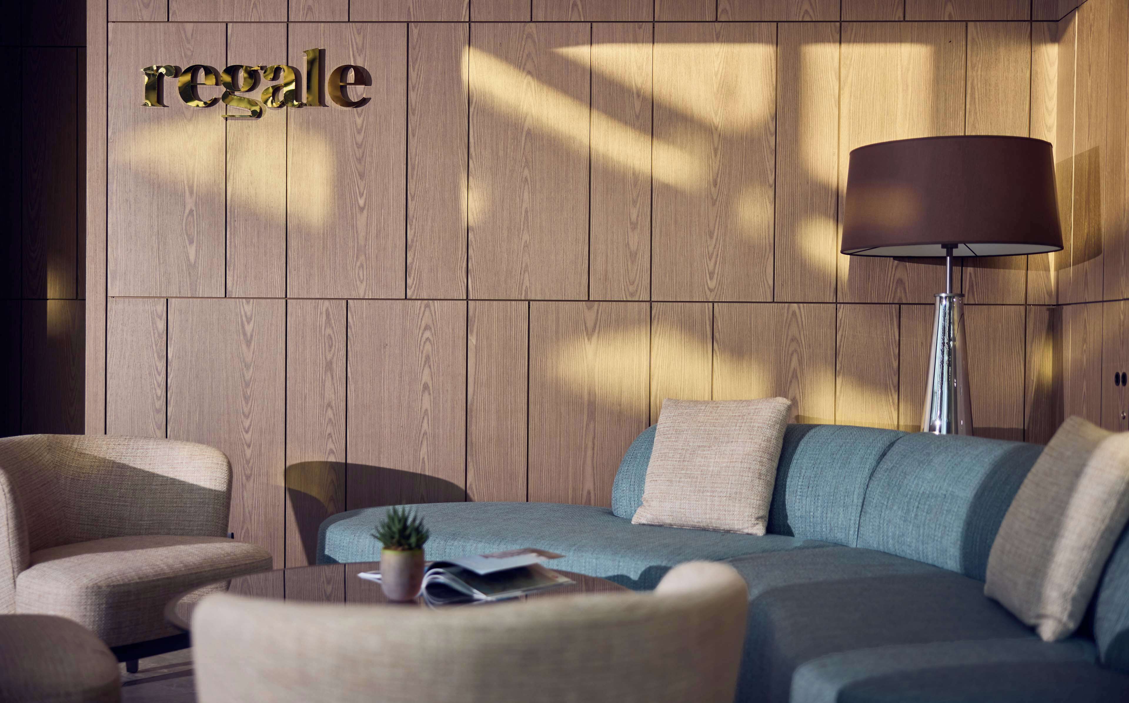 A modern living room with a wooden panel wall, a sofa, armchairs, a floor lamp, and a small potted plant.
