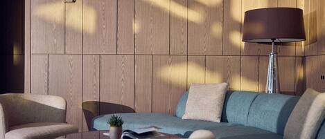 A modern living room with a wooden panel wall, a sofa, armchairs, a floor lamp, and a small potted plant.