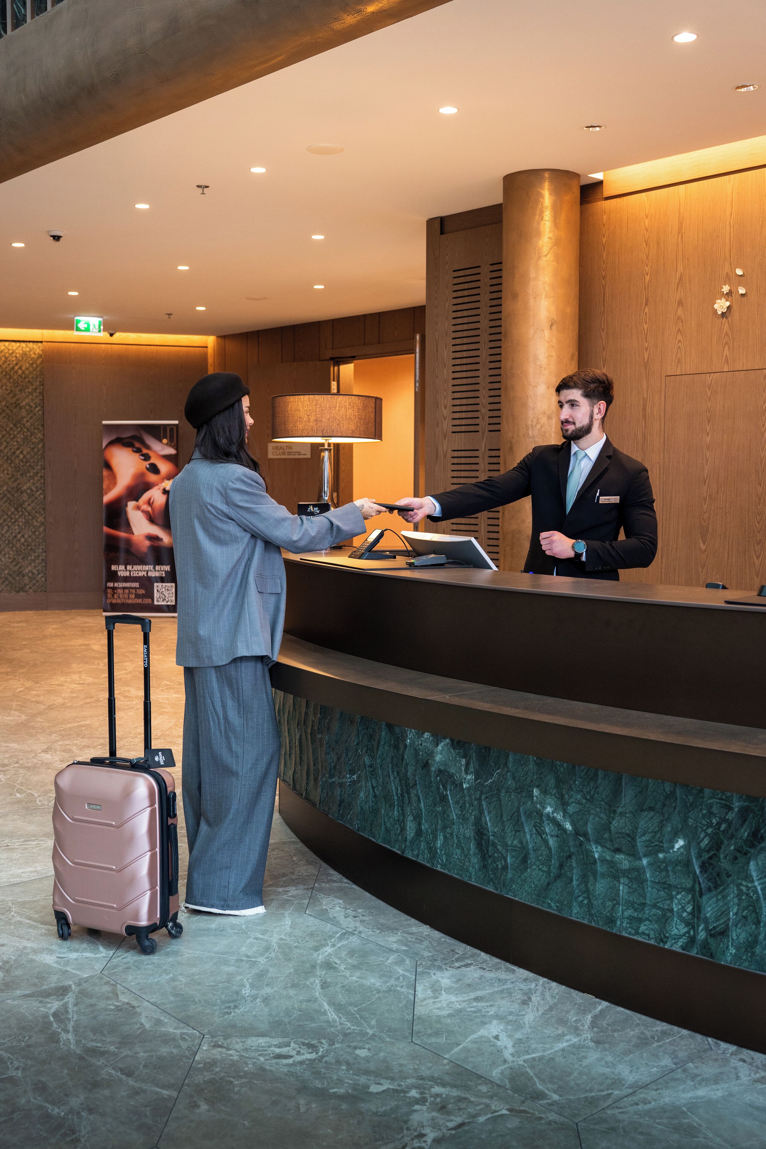 Ein Hotelrezeptionstresen mit einer Holzwand im Hintergrund, einer Rezeptionstheke und einem Boden mit Marmorfliesen.