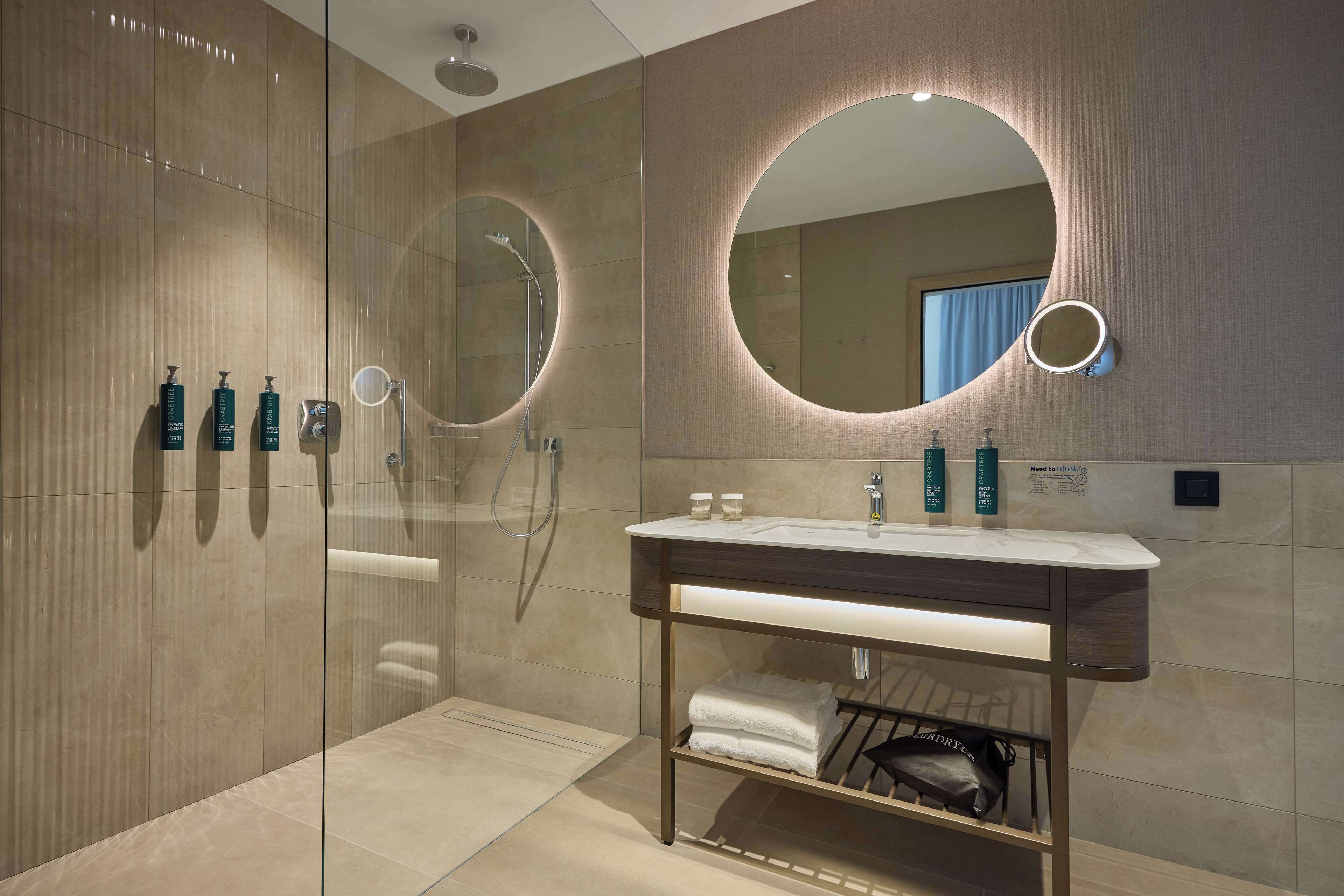 Et moderne badeværelse med en glasbrusekabine, et vaskebord med spejl og toiletartikler.