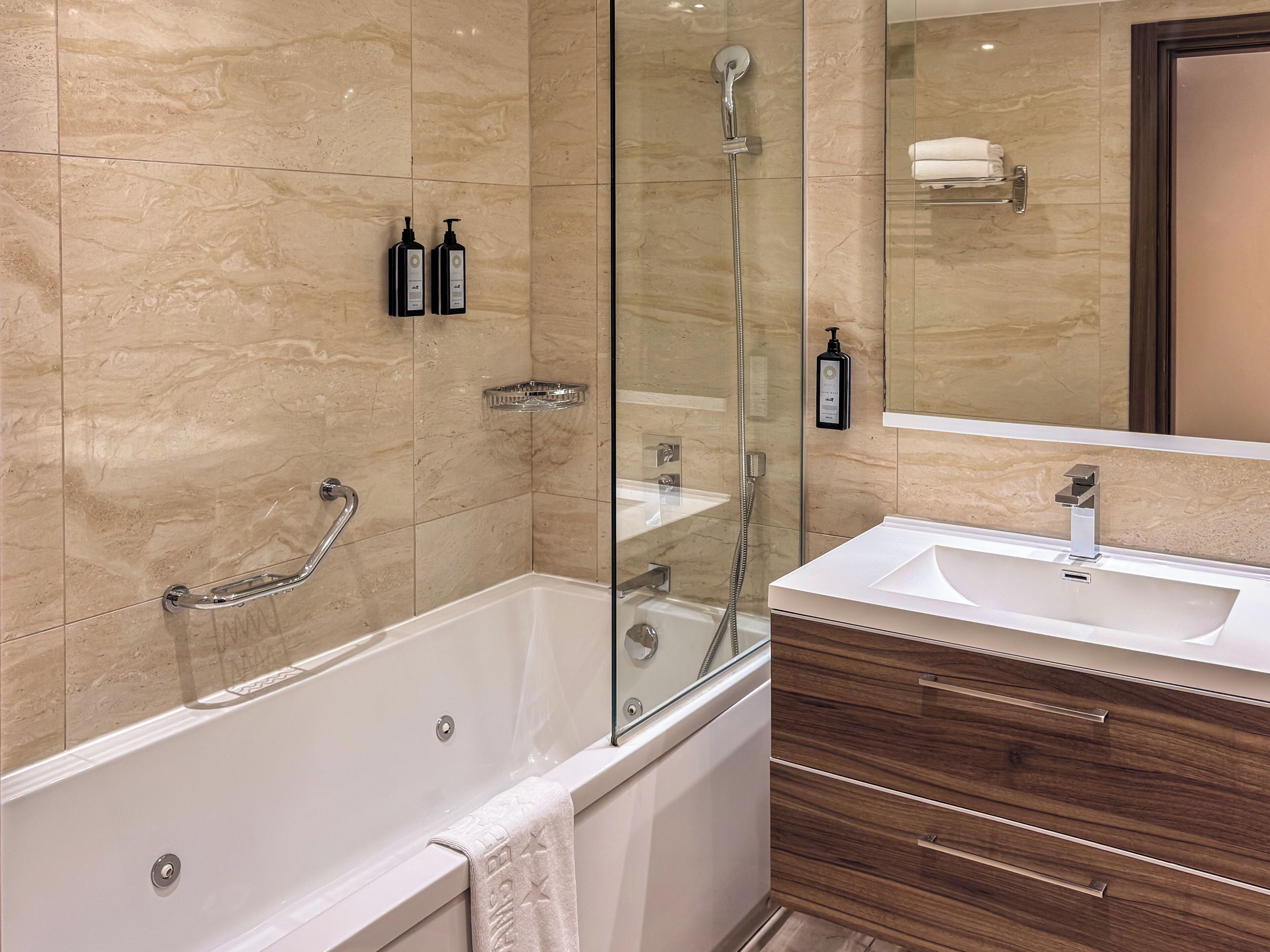 A modern bathroom with a glass-enclosed shower, a white bathtub, and a wooden vanity with a sink.