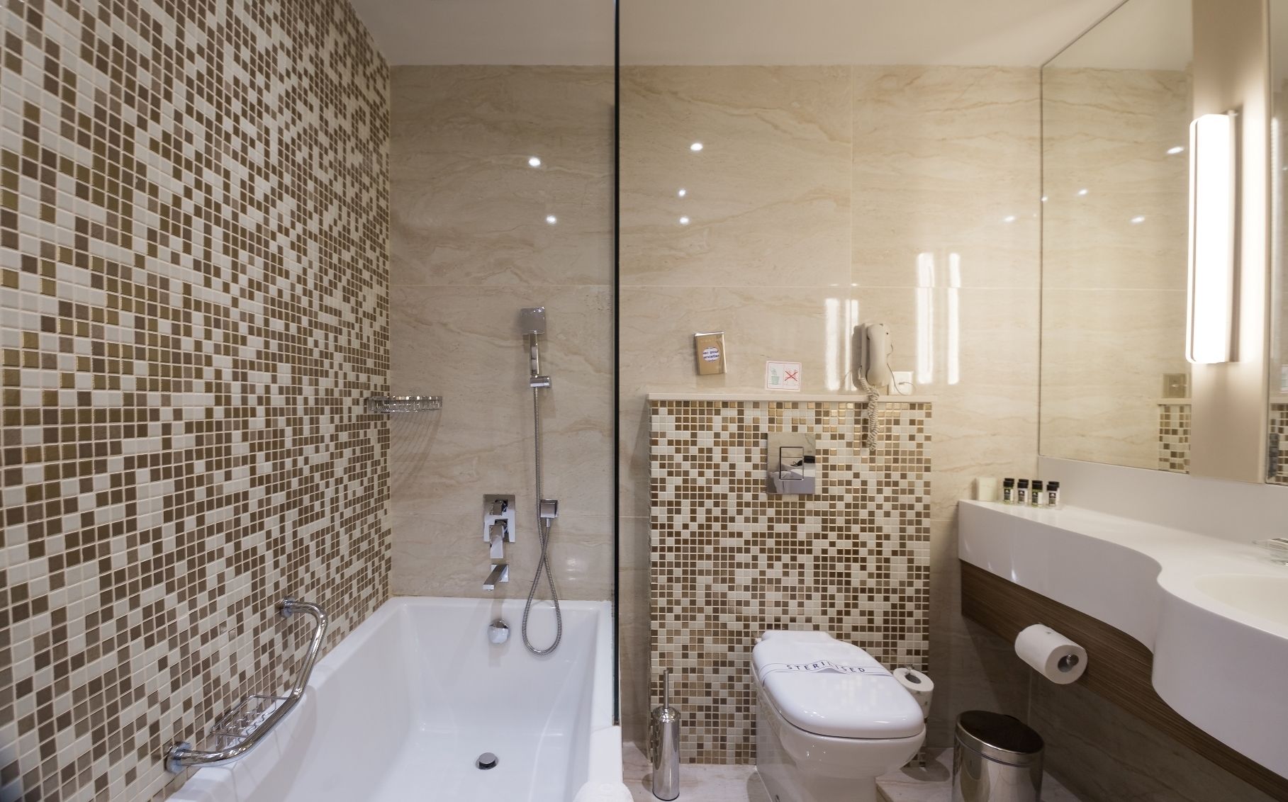 Un baño moderno con ducha de mosaicos, inodoro y tocador con espejo.