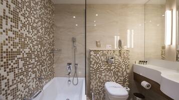 Un baño moderno con ducha de mosaicos, inodoro y tocador con espejo.