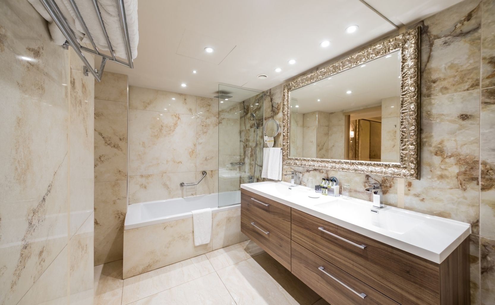 Un baño moderno con pared de mármol, un espejo grande, una bañera y muebles de madera.