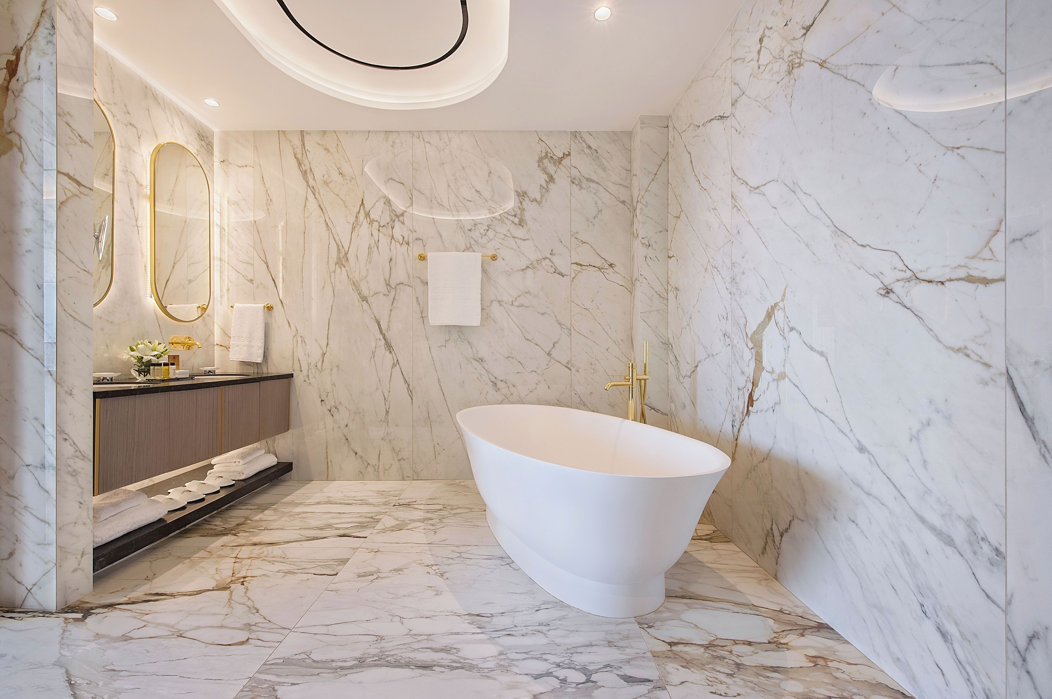 Un baño moderno con una bañera independiente, paredes de mármol y un tocador con espejo dorado.