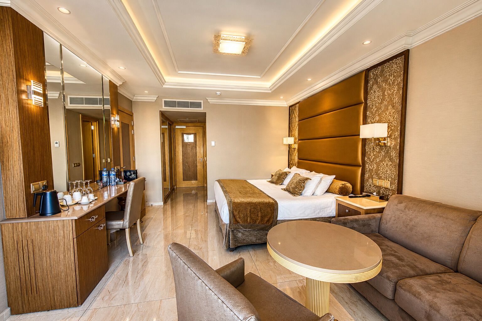 A hotel room with a bed, a sofa, a small table, a desk with a chair, and a large mirror.