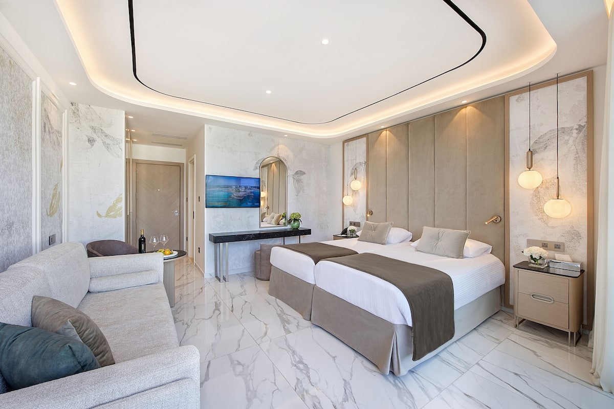 A modern hotel room with a large bed, a sofa, a desk, and a bathroom visible through an archway.